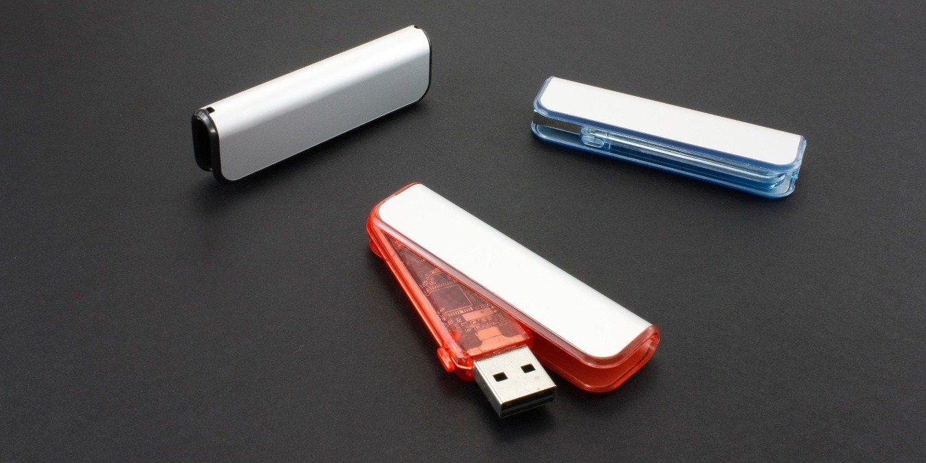 Three custom swivel cap USB drives in different colors on a grey surface