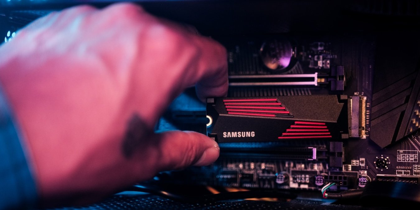 Close-up of a hand holding an M.2 SSD near a motherboard